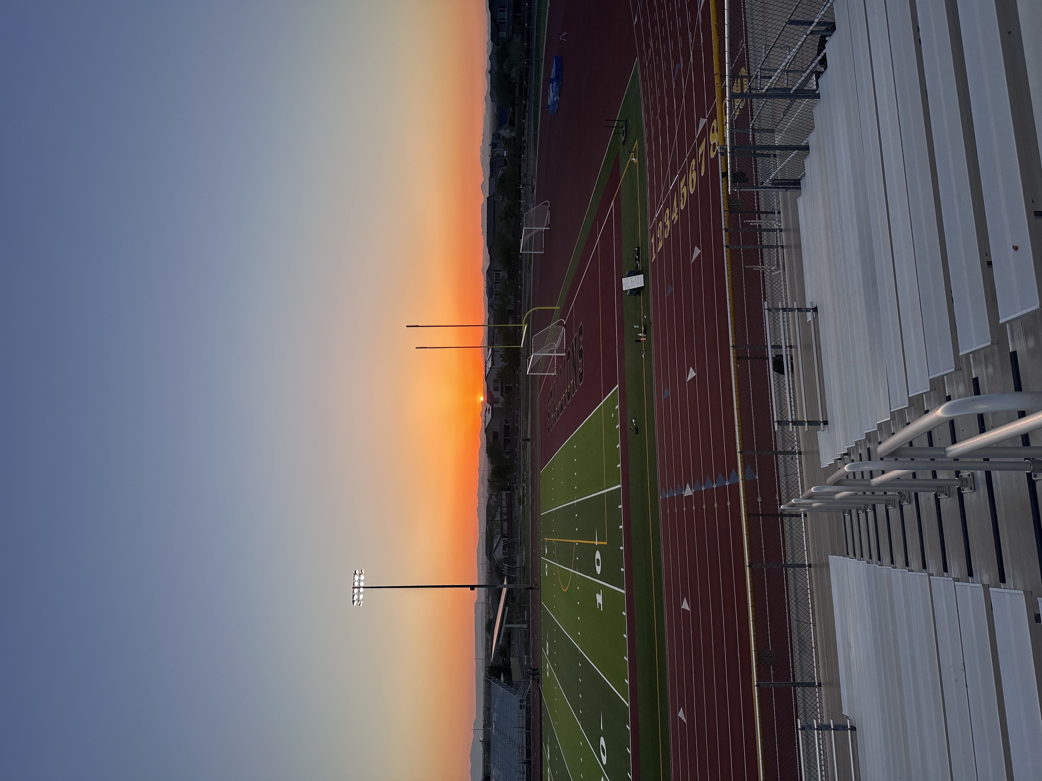 sun setting behind football goalposts over red running track