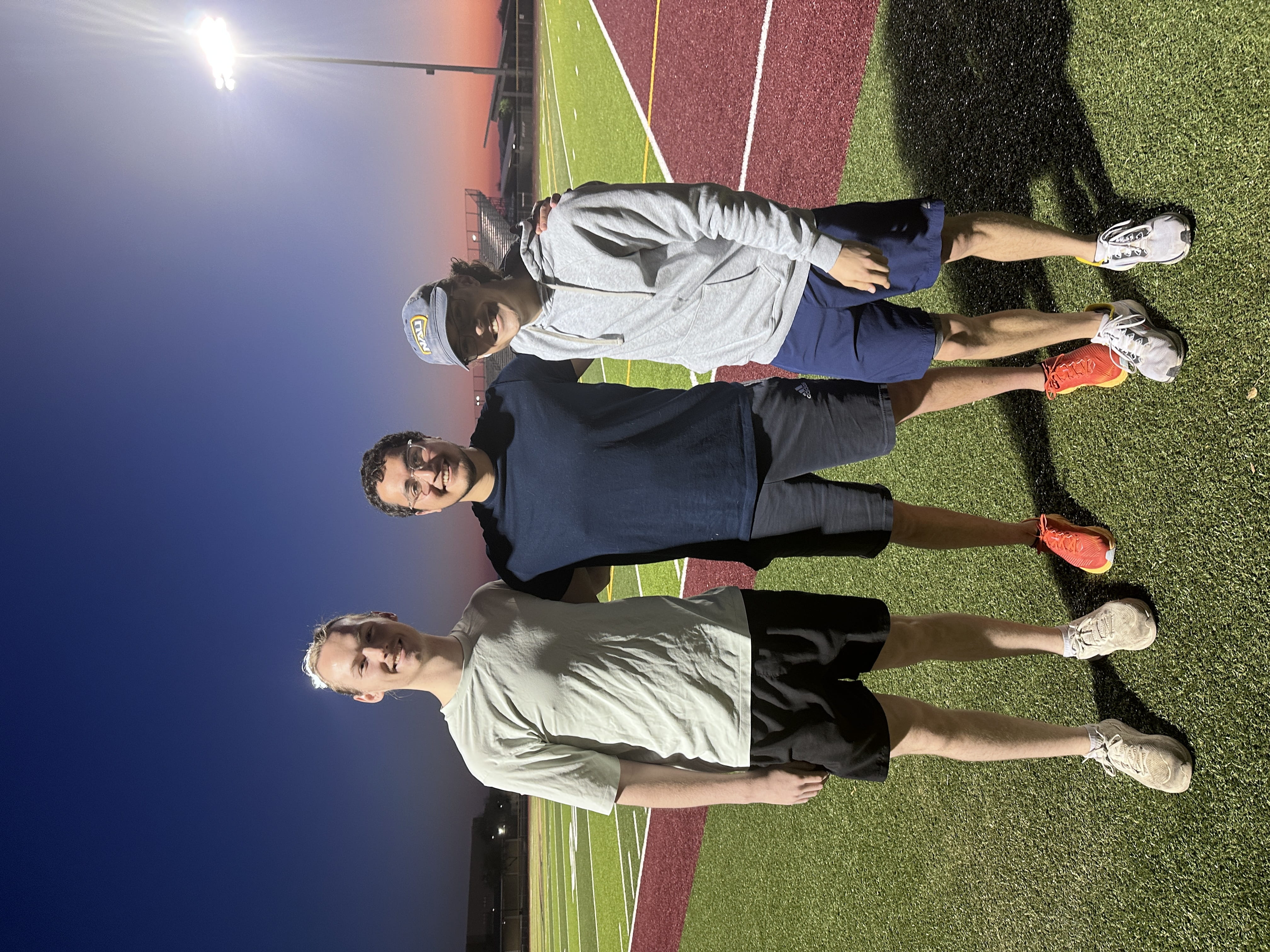three people standing on a lit sports field at sunset