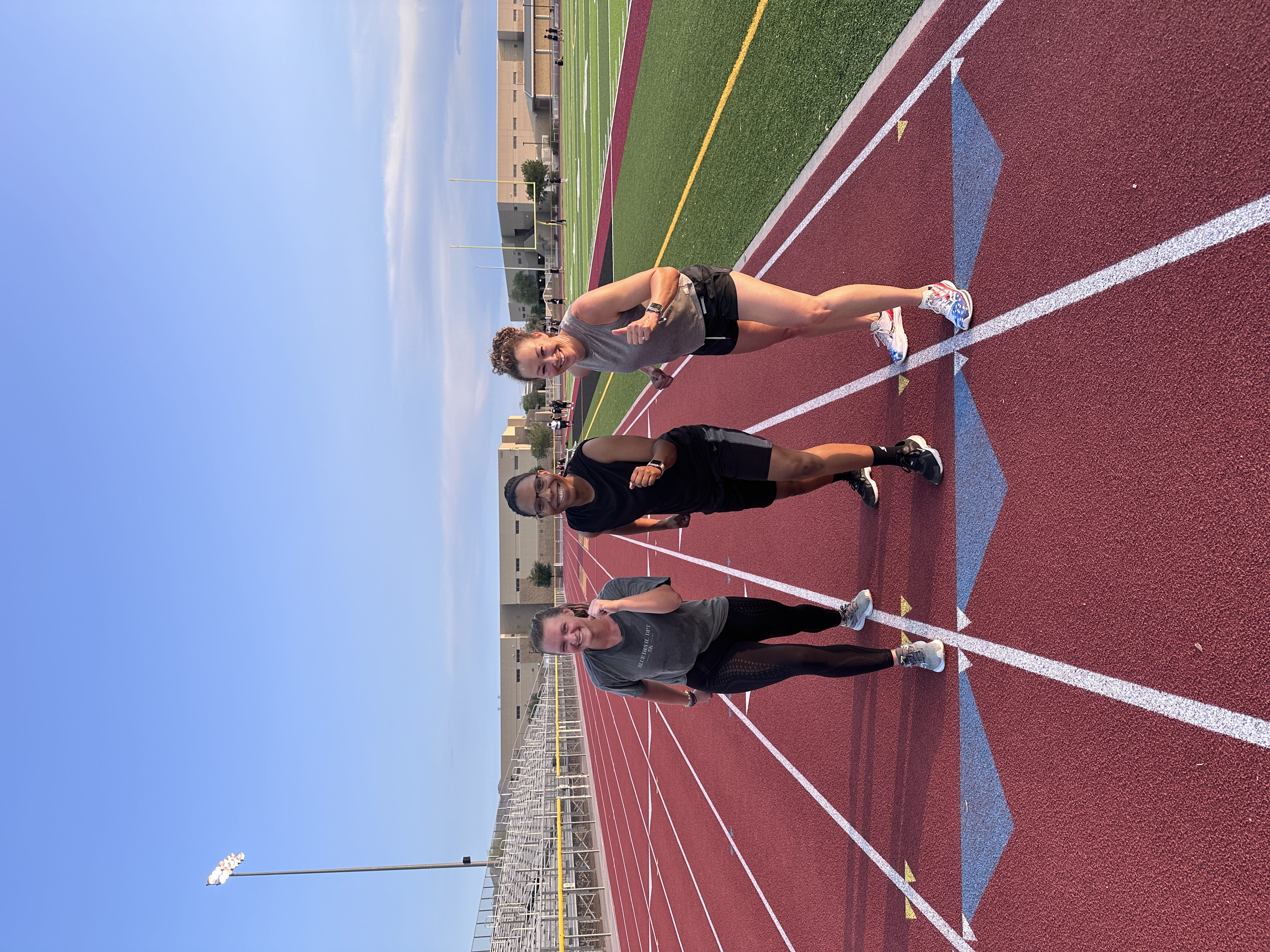 three women posing in running stance on track in daylight