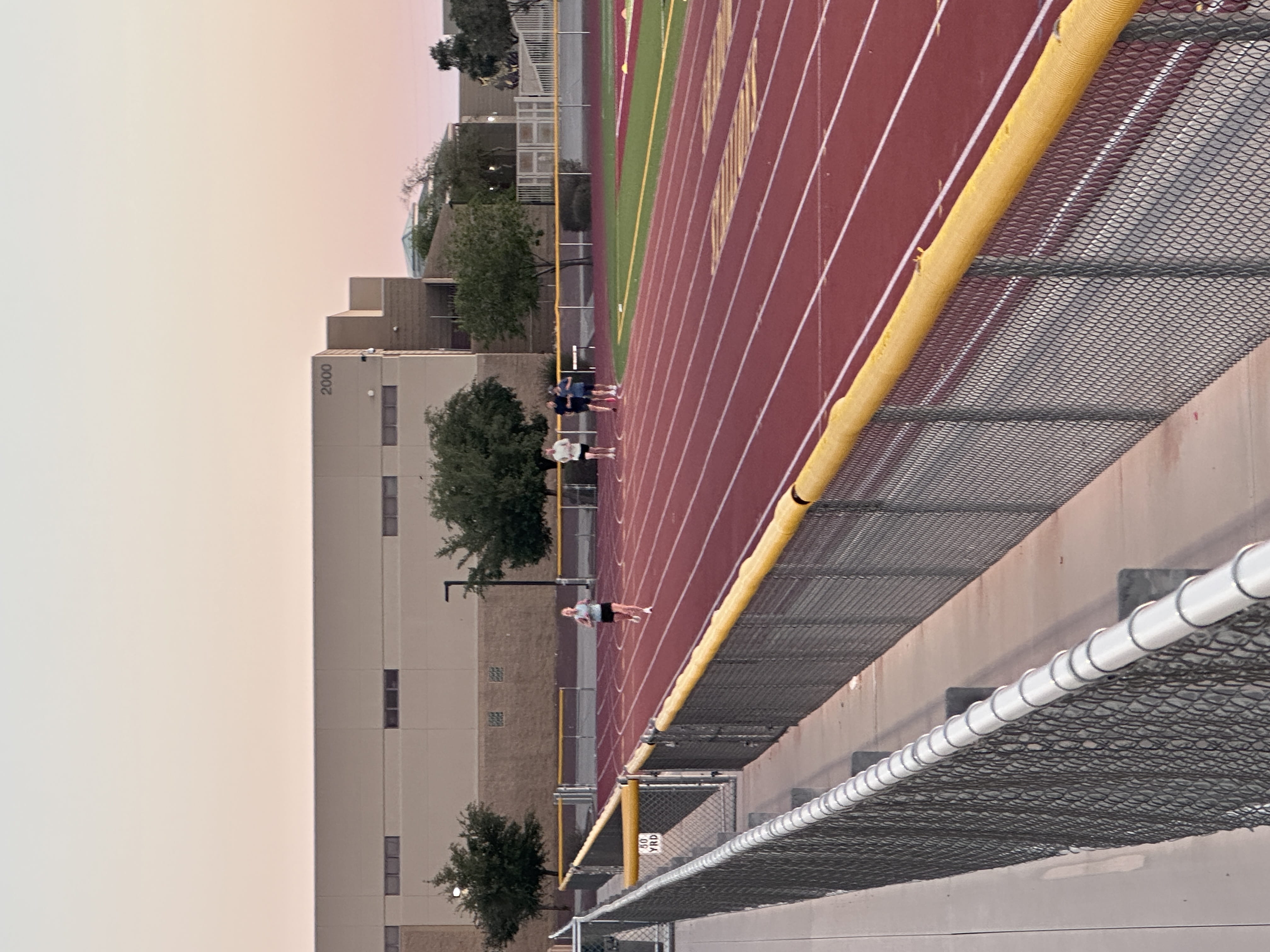 people jogging on a red track near school buildings at sunrise